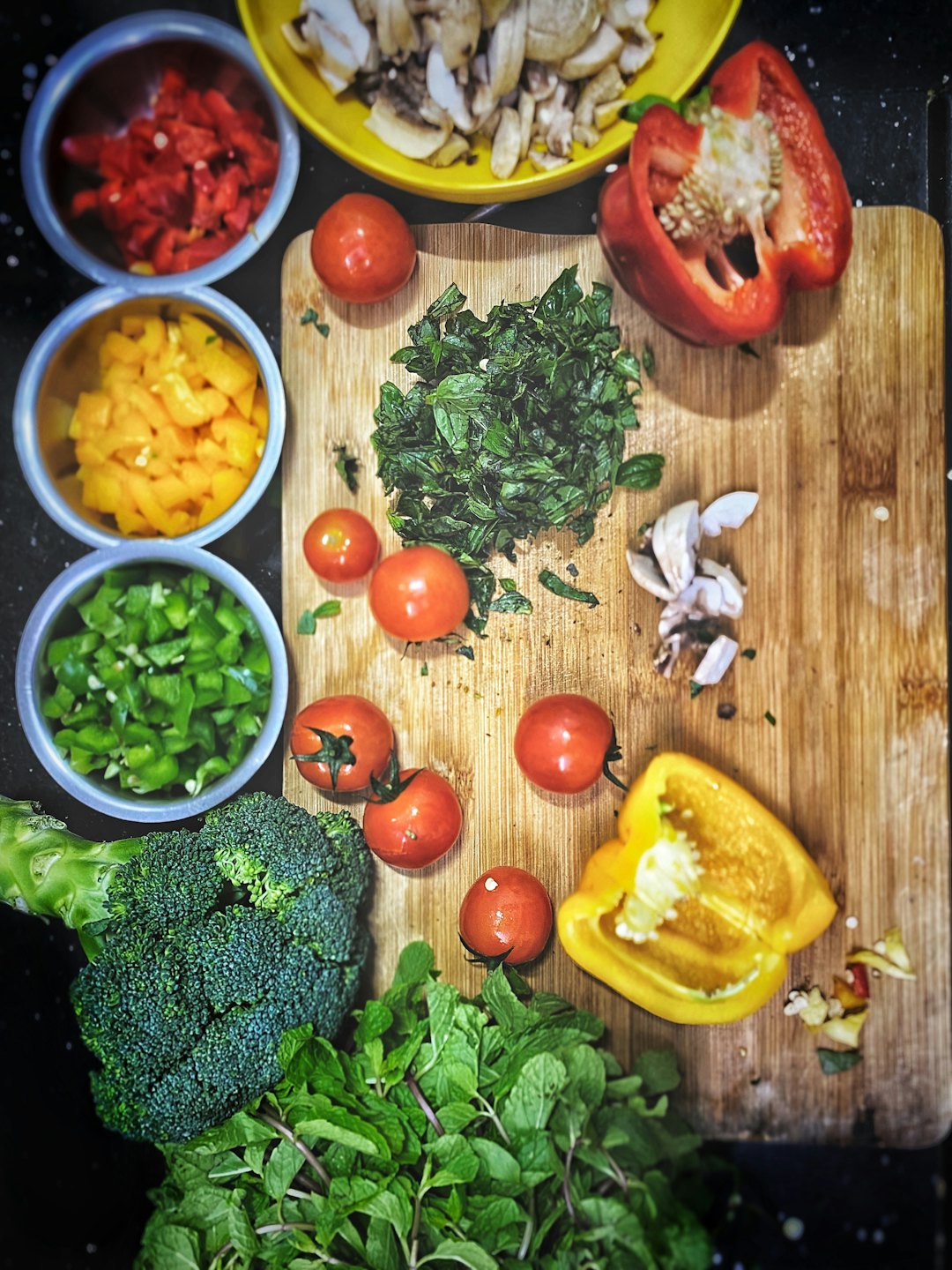 Colorful prepped vegetables and herbs on a dark counter.