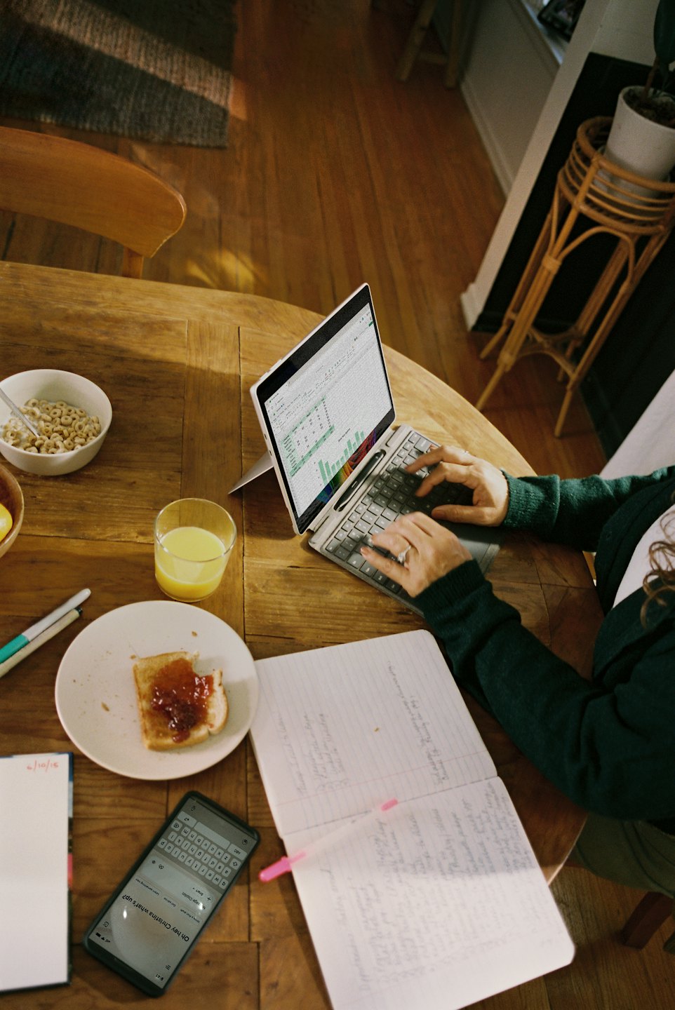 Hands typing on a laptop with breakfast items on a wooden table.
