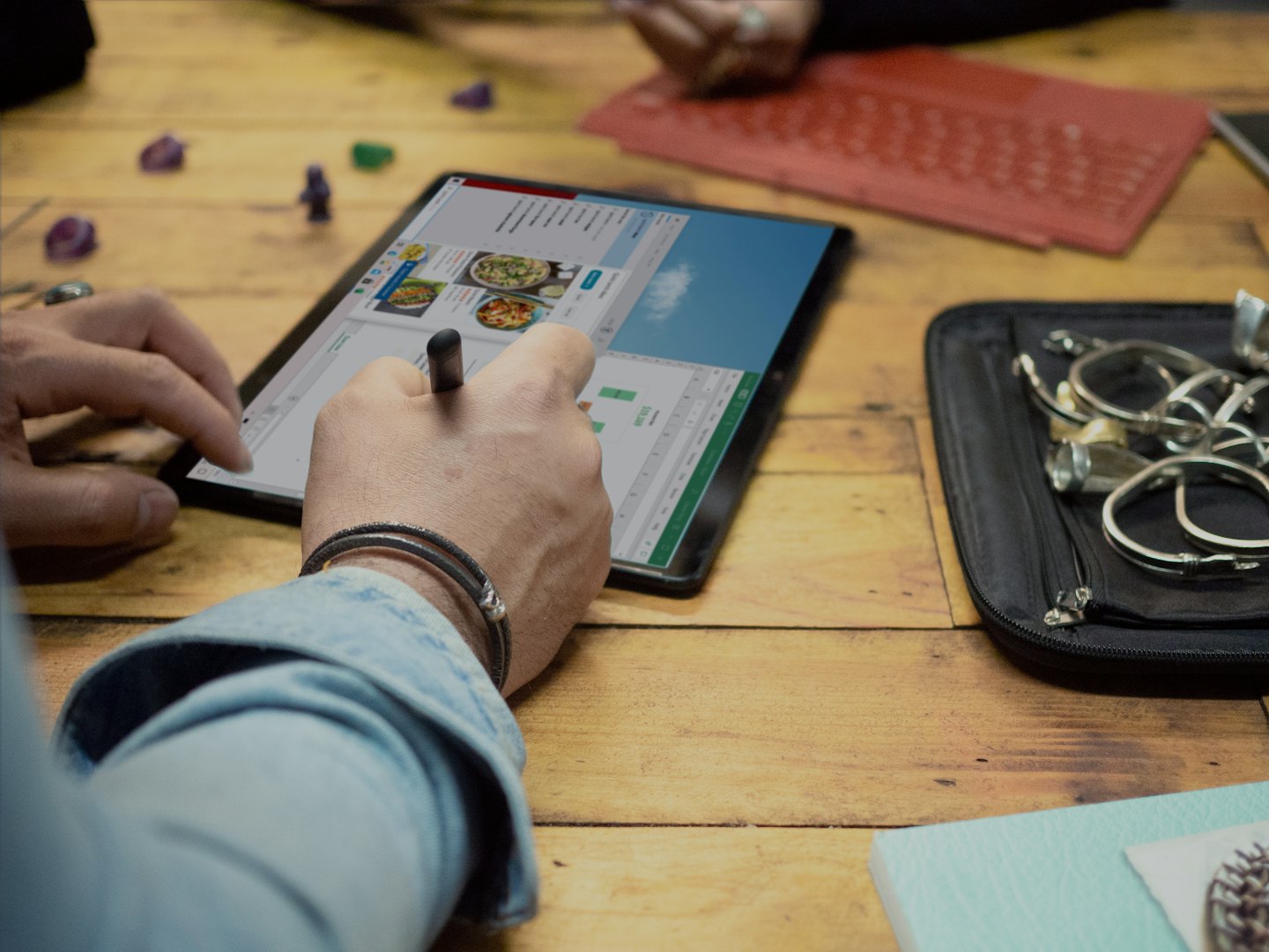 Hands using a stylus to navigate a recipe tablet.