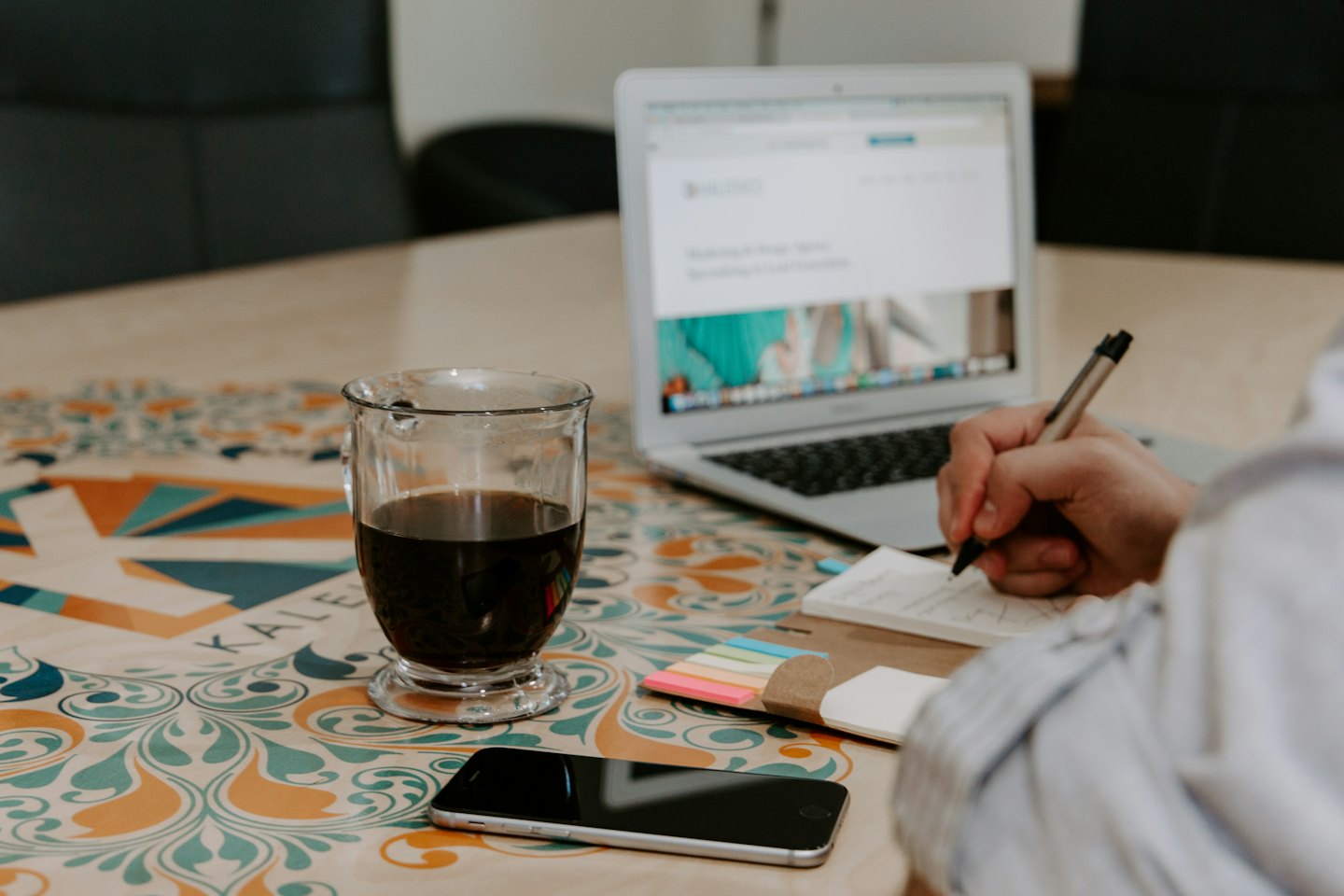 Hand writing in notebook with laptop and coffee on table.