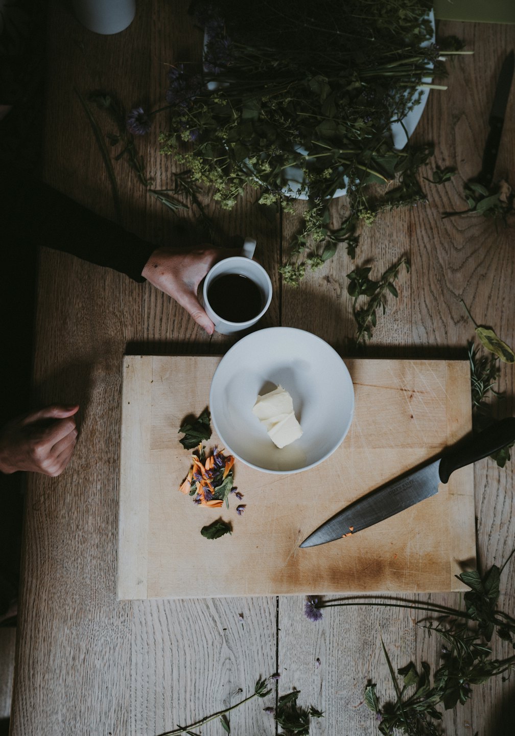 Hands prepare fresh herbs and flowers on a wooden table.
