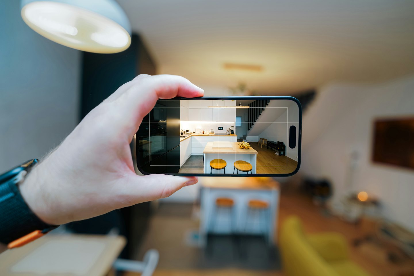 Hand holding black smartphone showing a modern kitchen interior.